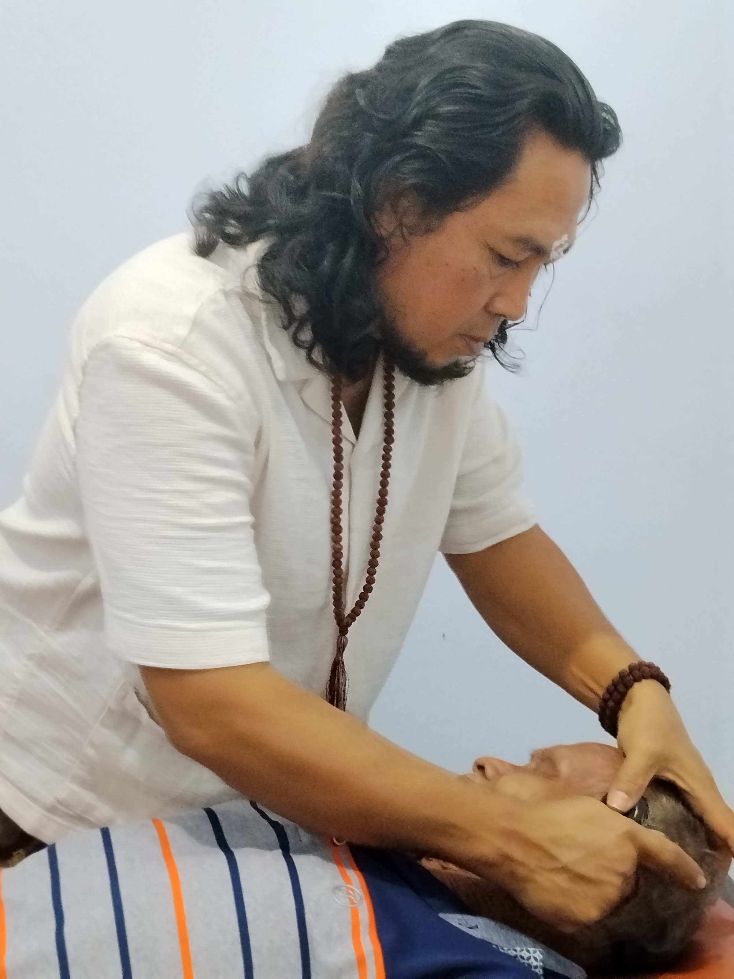 JRO in profile, his hands supporting an elderly client's head during a treatment, his expression calm and focused.