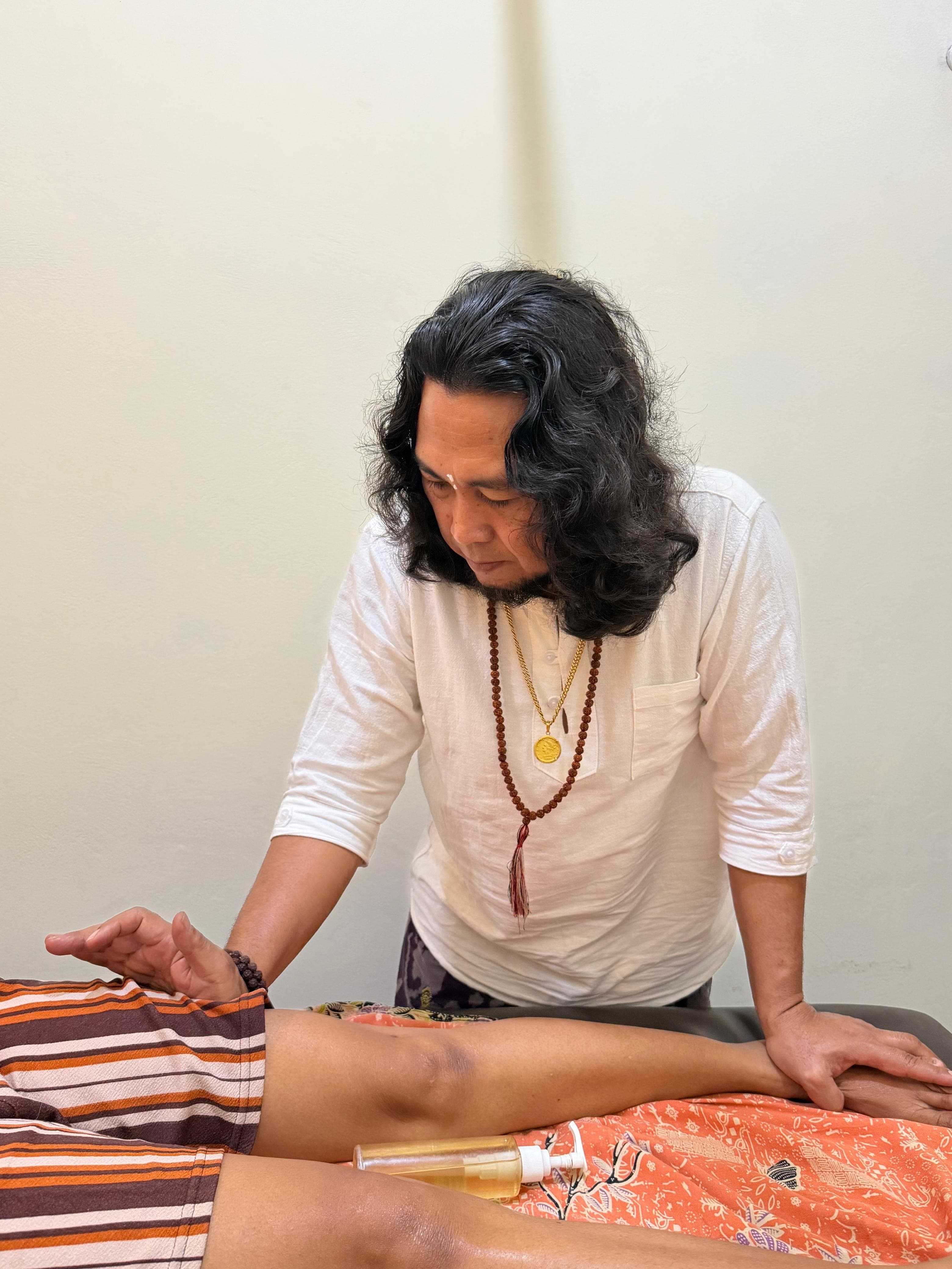 JRO standing at the treatment table, working with both hands on a client’s legs during a session.