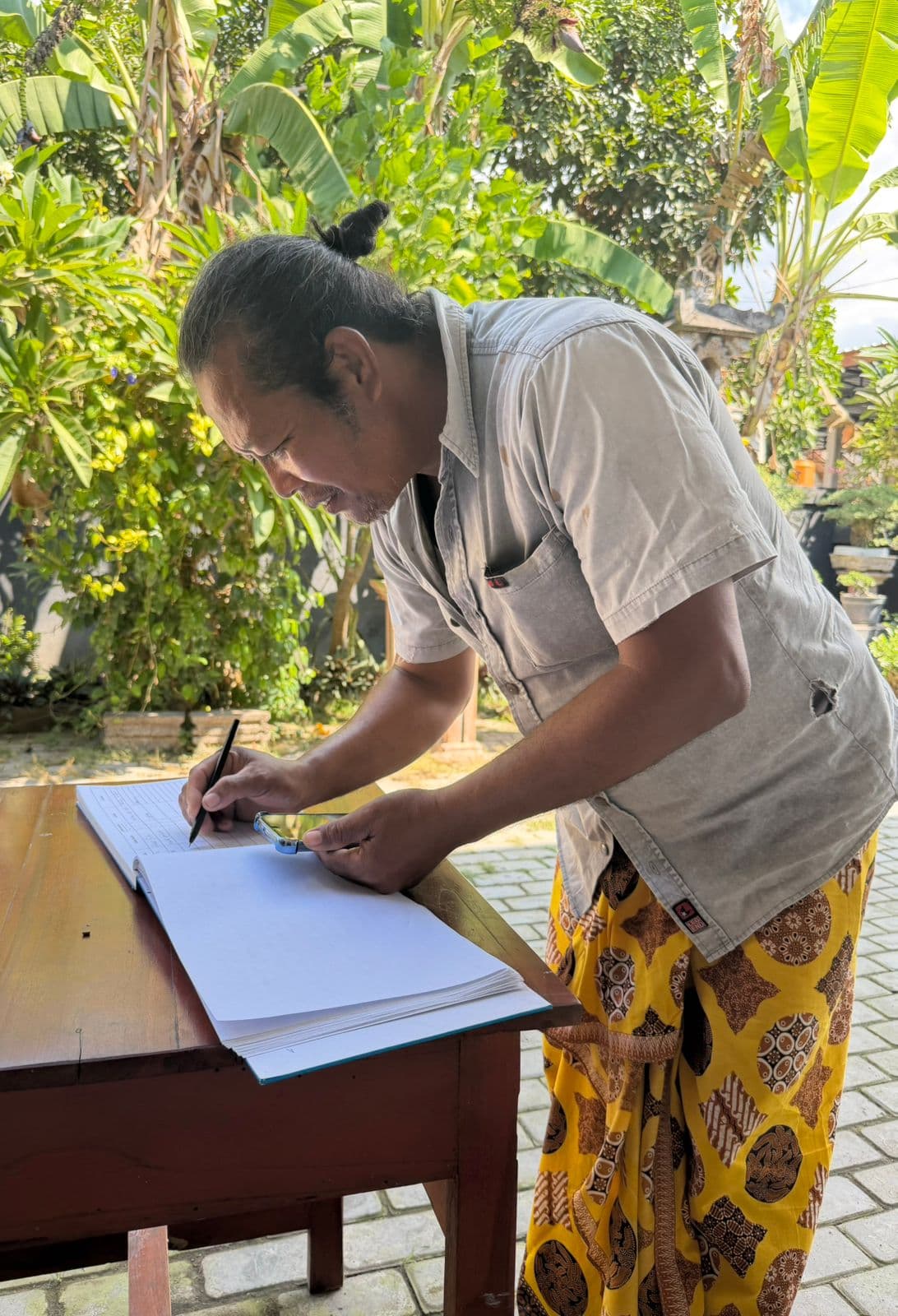A client writing their details into the Buku Pasien, the official patient register.